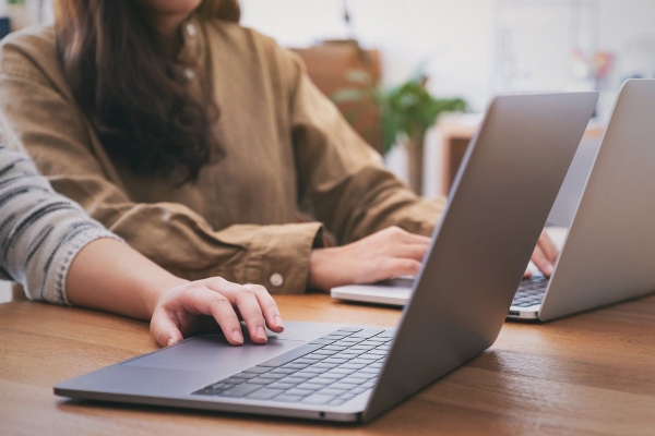 Two colleagues working side by side on laptops at a wooden desk